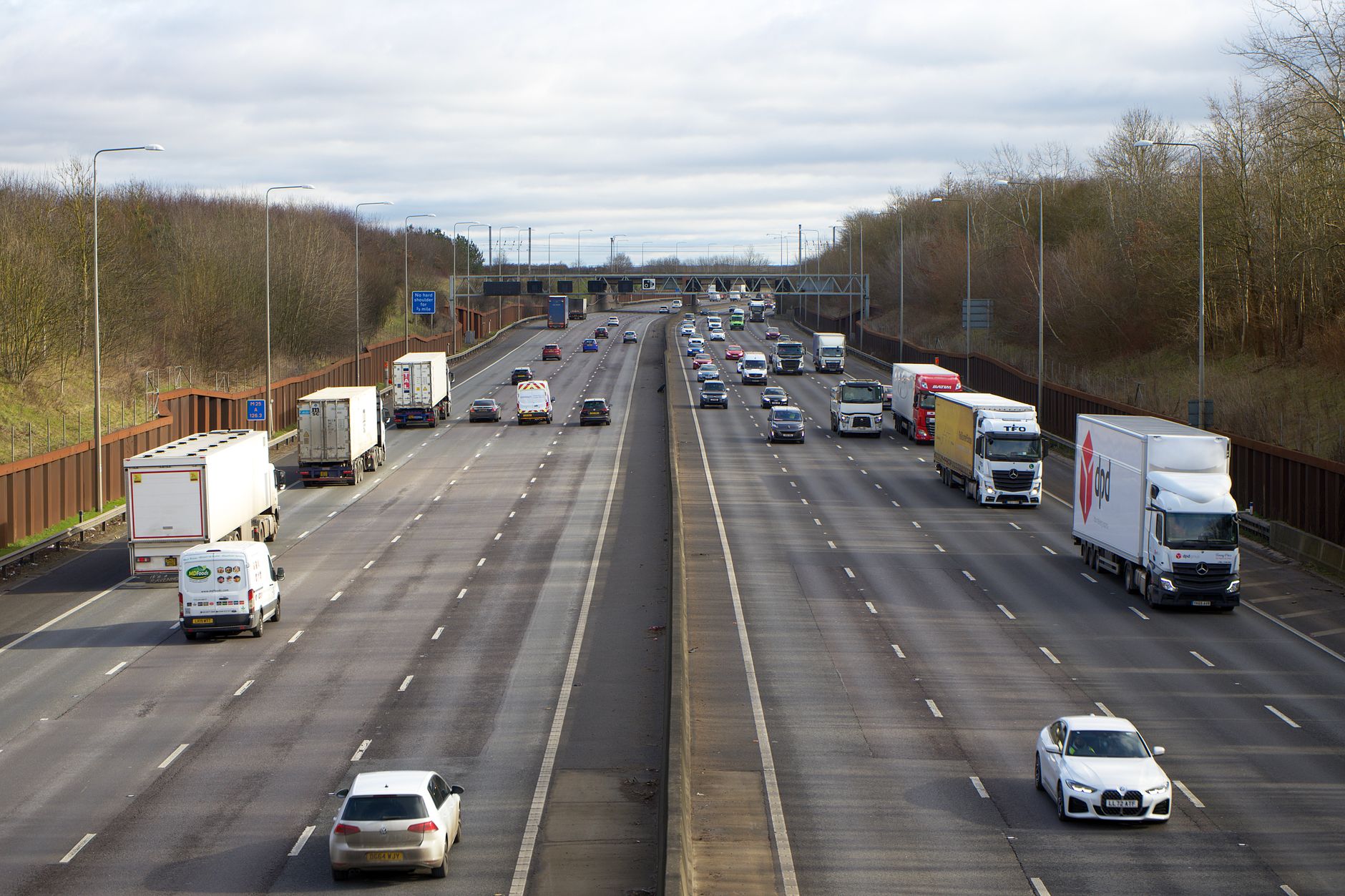 Busy motorway with cars and trucks moving in both directions between wooded verges